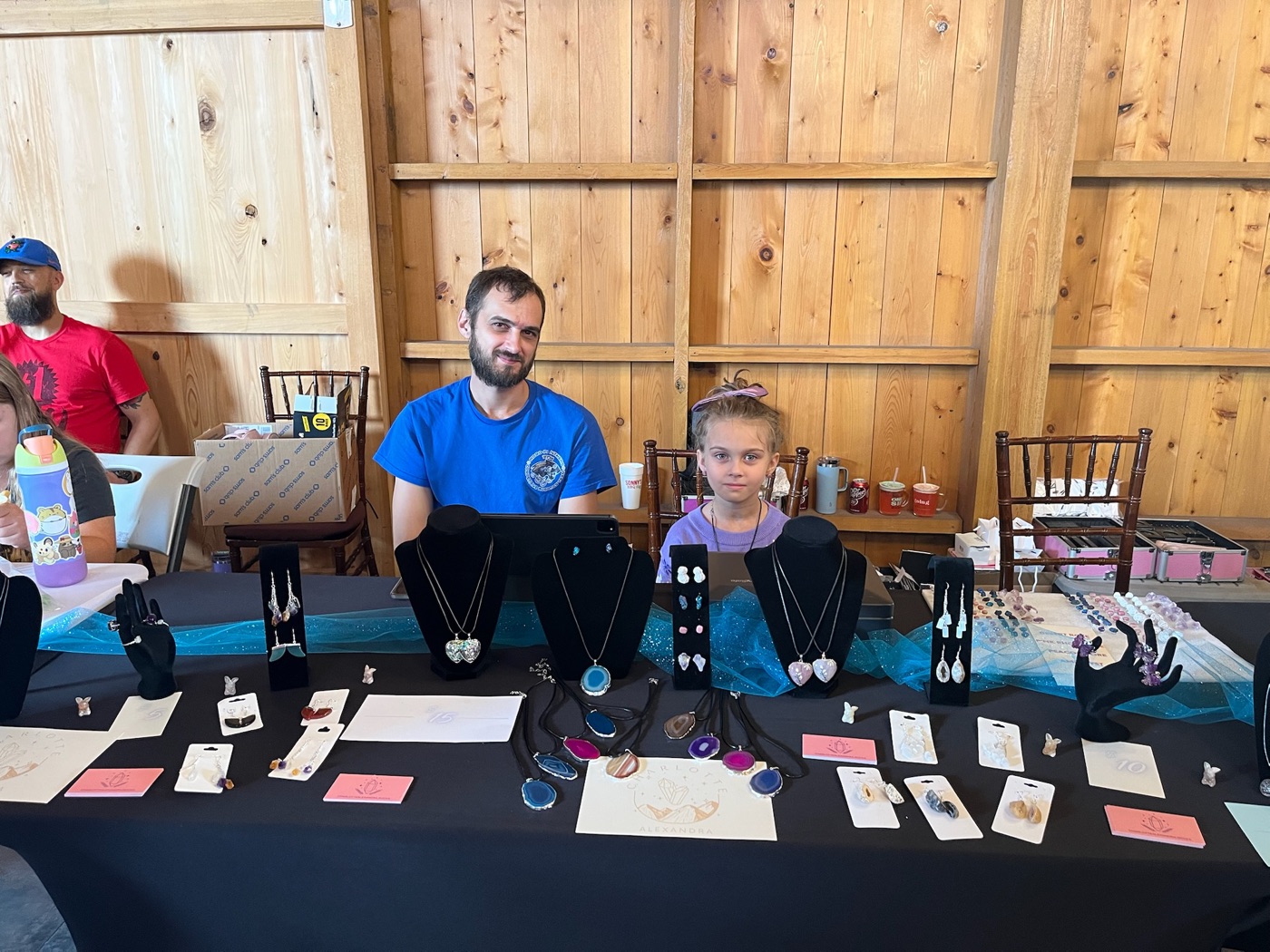 Charlie at her jewelry booth, surrounded by necklaces, earrings, and gemstones